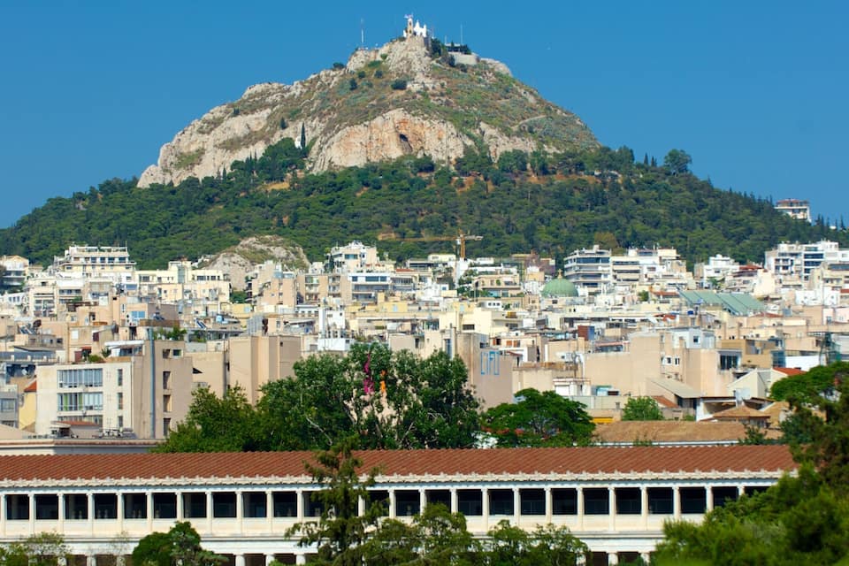 A cityscape with a prominent hill featuring a statue, surrounded by dense urban buildings.