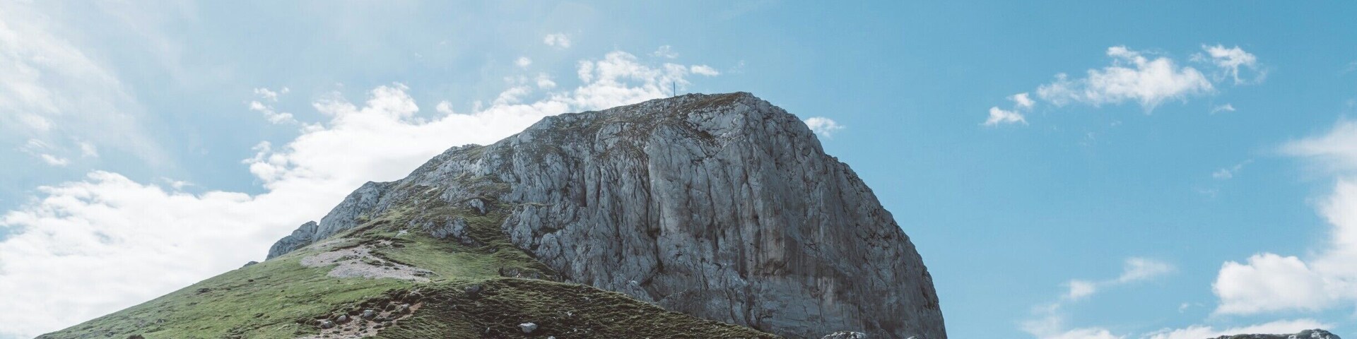 A mountain with a rocky peak and a grassy trail.