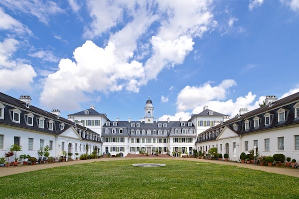 A large white building with a central tower, surrounded by a well-maintained lawn and potted plants.