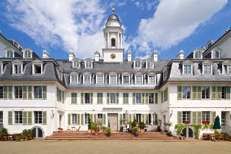 A large white building with green shutters, a clock tower, and a symmetrical facade.