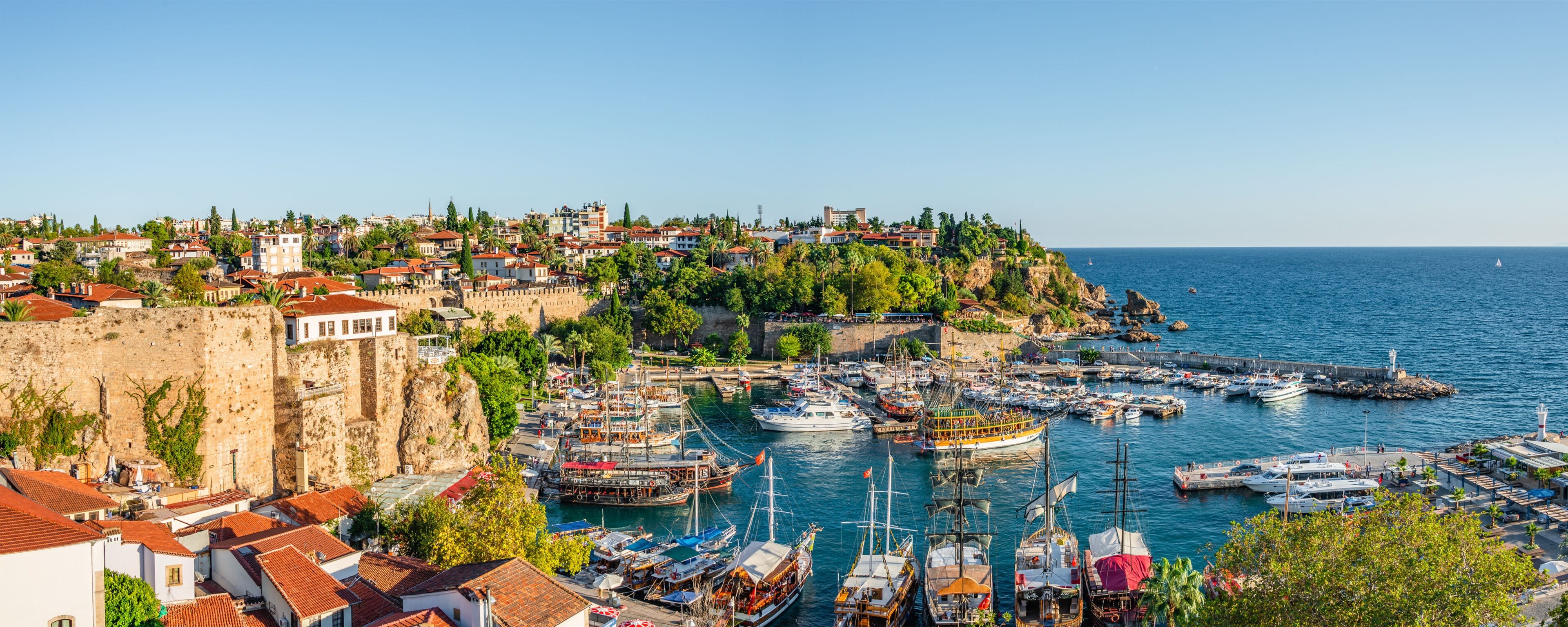 A coastal town with a historic fort, a marina with various boats, and a clear blue sea.