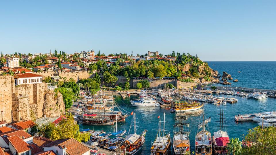 A coastal town with a historic fort, a marina with various boats, and a clear blue sea.