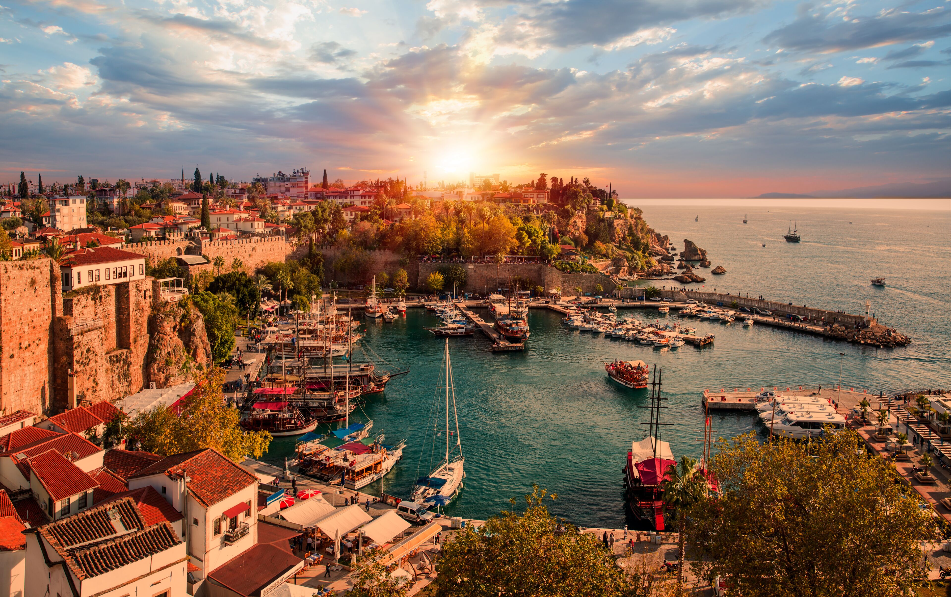 A coastal town with a historic fort, a marina with boats, and a sunset over the sea.
