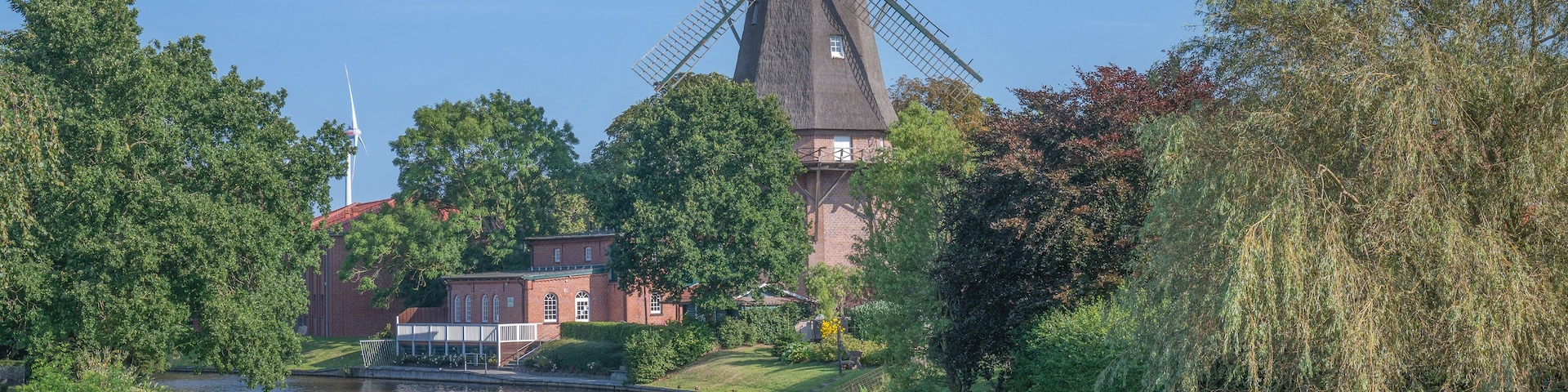 Un molino tradicional junto a un río, rodeado de exuberante vegetación y un edificio de ladrillo.