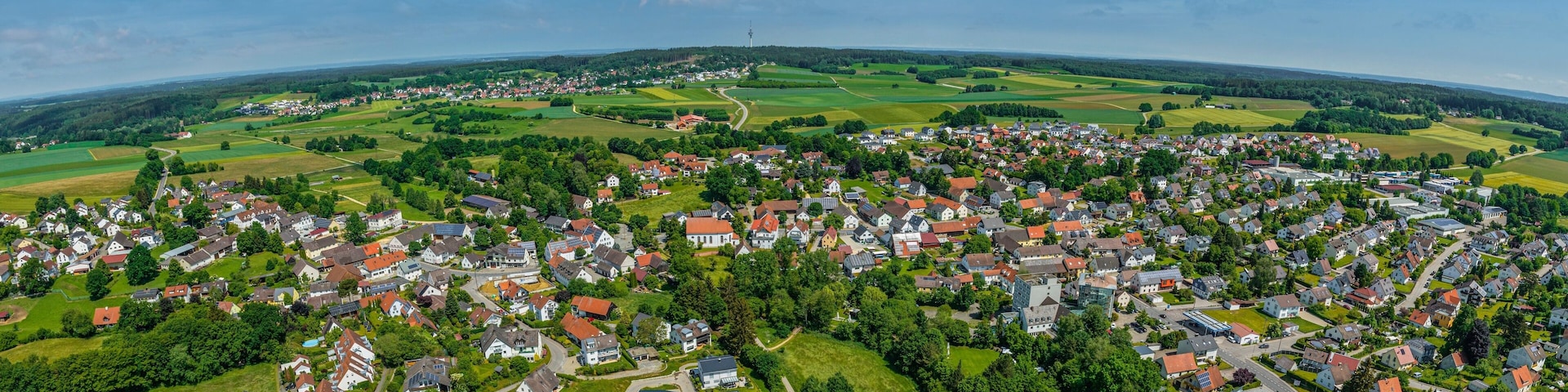 An aerial view of a town surrounded by green fields and a distant tower.