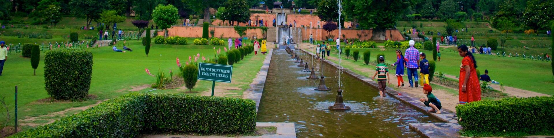 A park with a water feature, lush greenery, and mountains in the background.