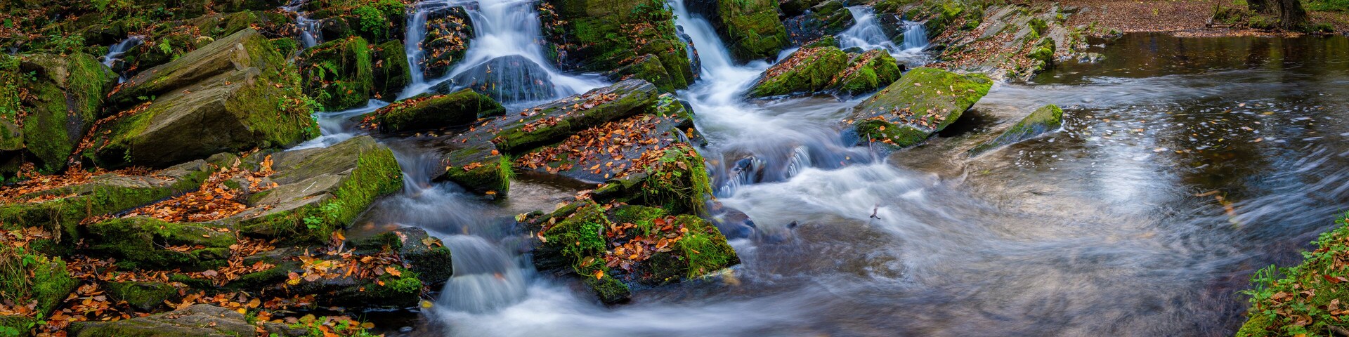 A waterfall cascading over moss-covered rocks in a forested area.