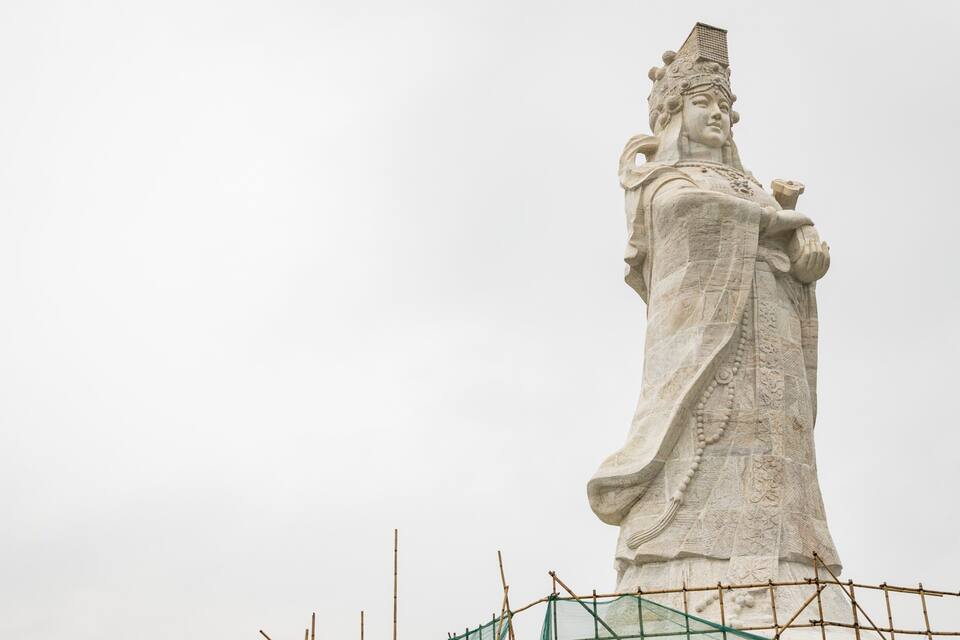 A large stone statue with intricate carvings, a headdress, and a raised hand.