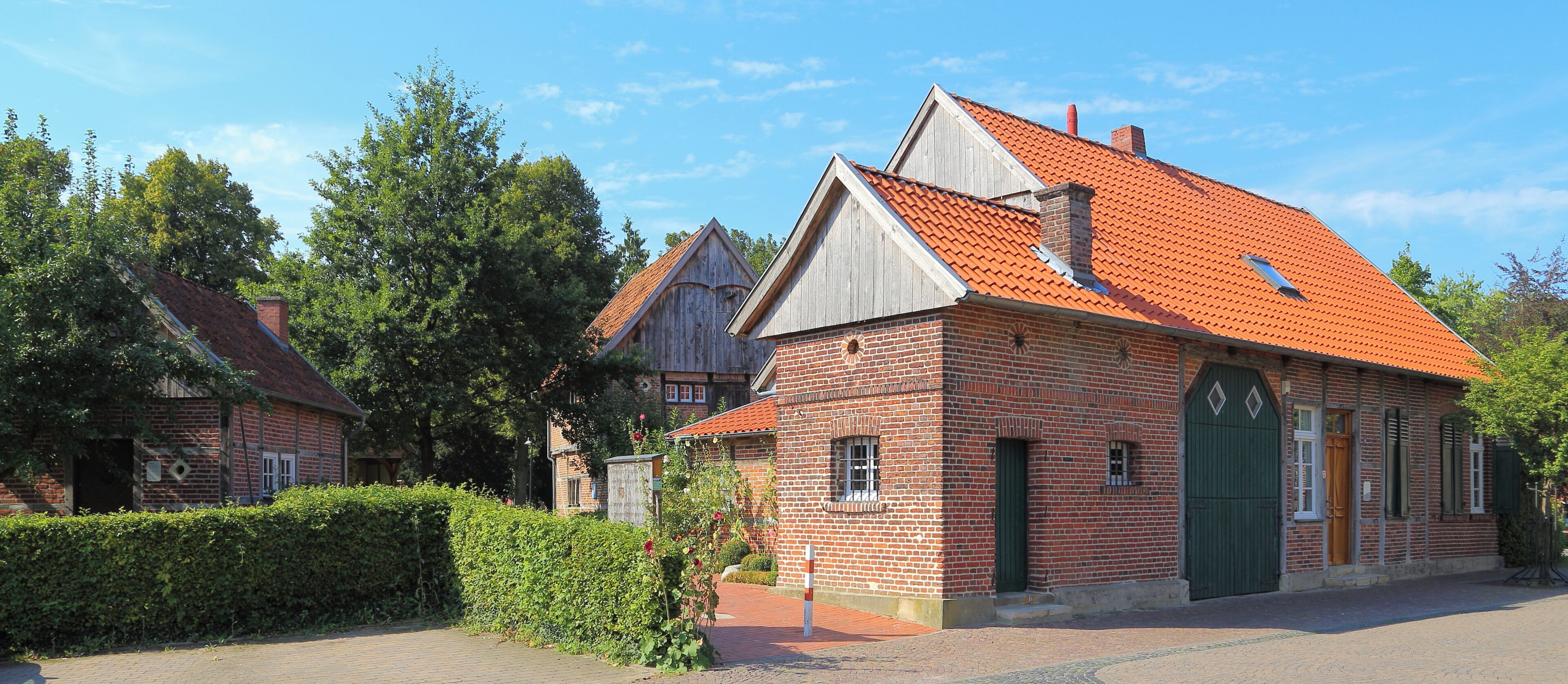 A brick building with a red-tiled roof, a green door, and a small window.