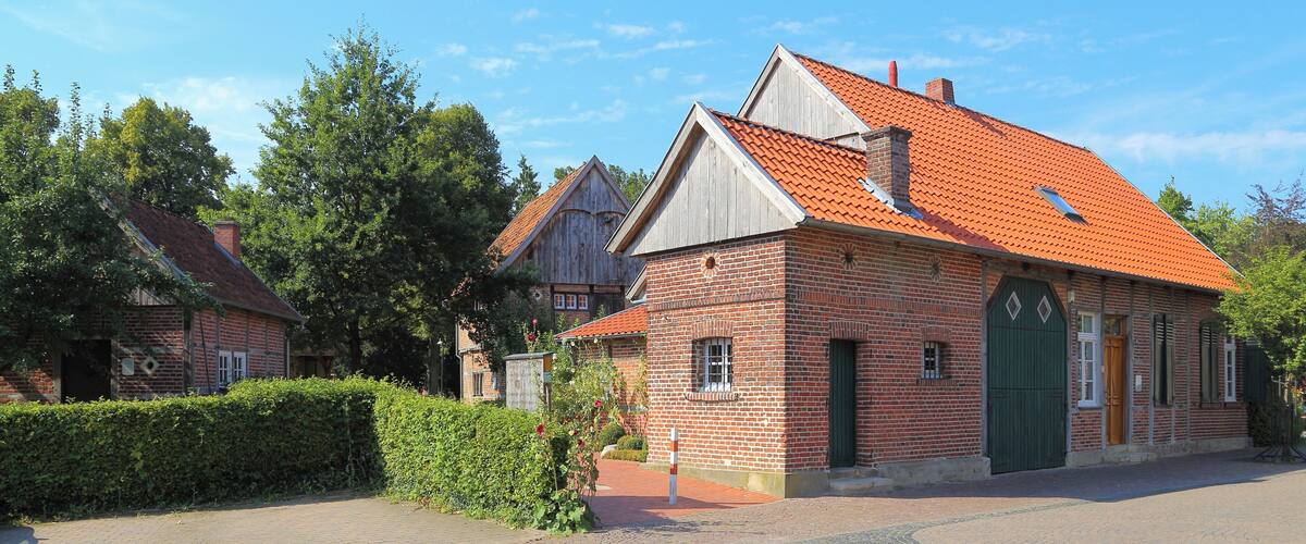 A brick building with a red-tiled roof, a green door, and a small window.