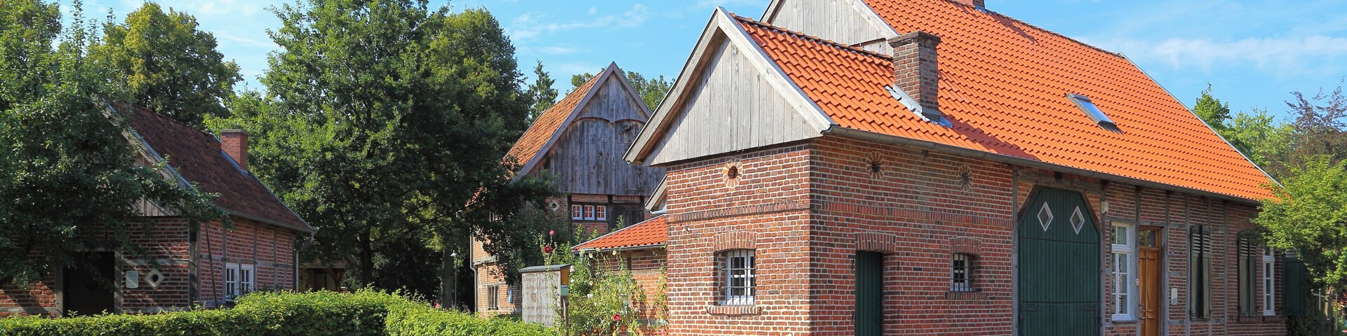 A brick building with a red-tiled roof, a green door, and a small window.
