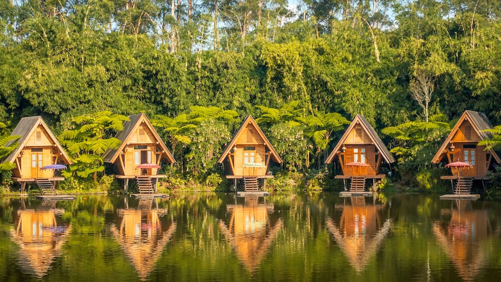 Wooden houses on stilts over a calm lake, surrounded by dense green forest.
