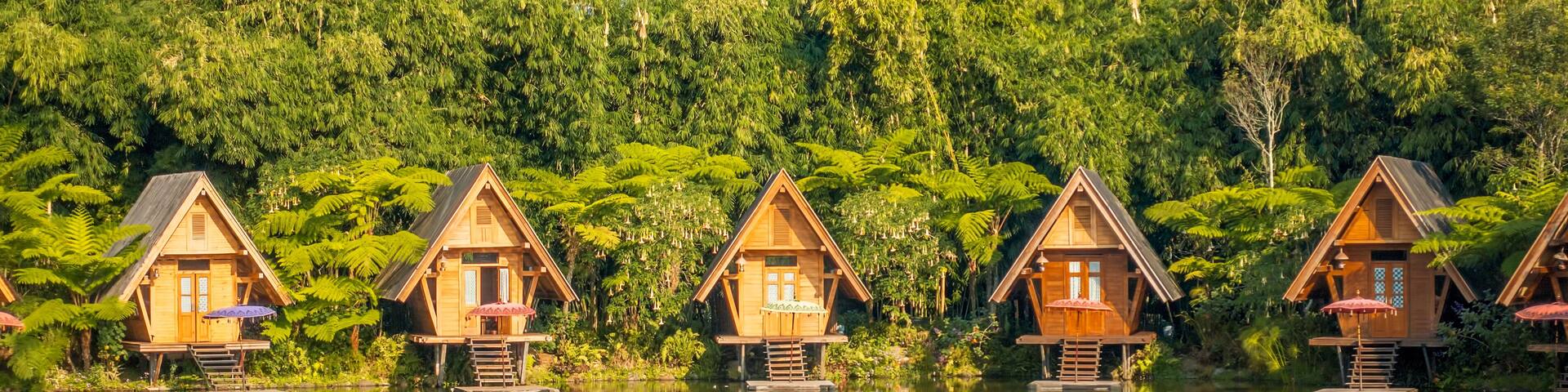 Wooden houses on stilts over a calm lake, surrounded by dense green forest.