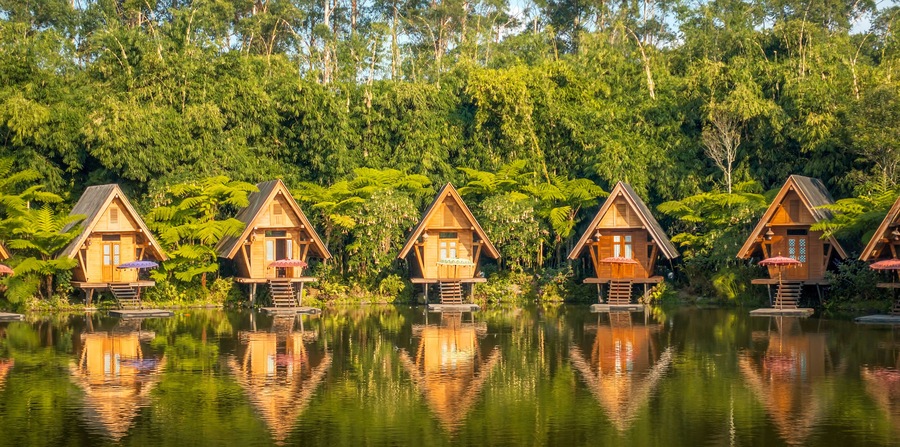 Wooden houses on stilts over a calm lake, surrounded by dense green forest.