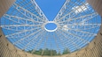 A large, circular glass roof structure with a central opening, supported by a metal framework.
