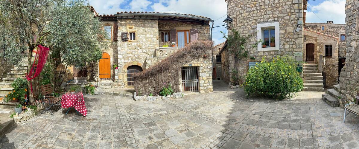 A stone courtyard with a wooden bench, potted plants, and a small tree.