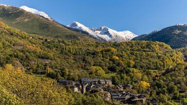 A mountainous landscape with snow-capped peaks, a village with traditional architecture, and dense forested hills.