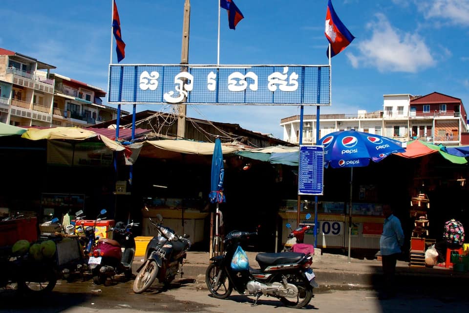 A street market with a signboard, motorcycles, and a Pepsi umbrella.