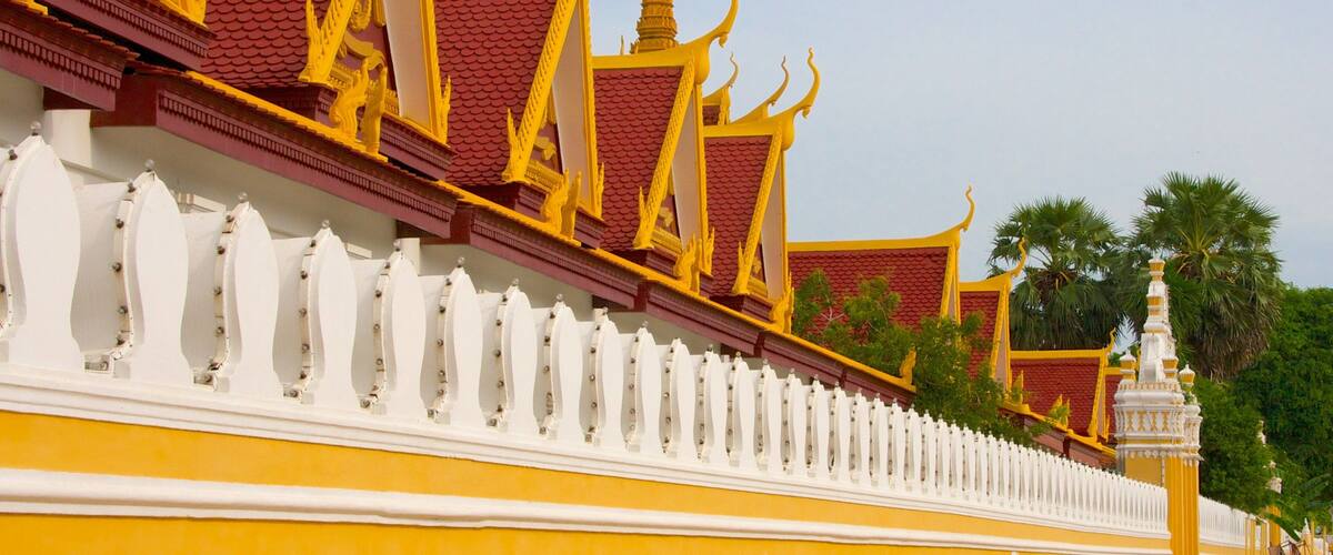 A traditional Thai temple with ornate golden roofs and a white fence.