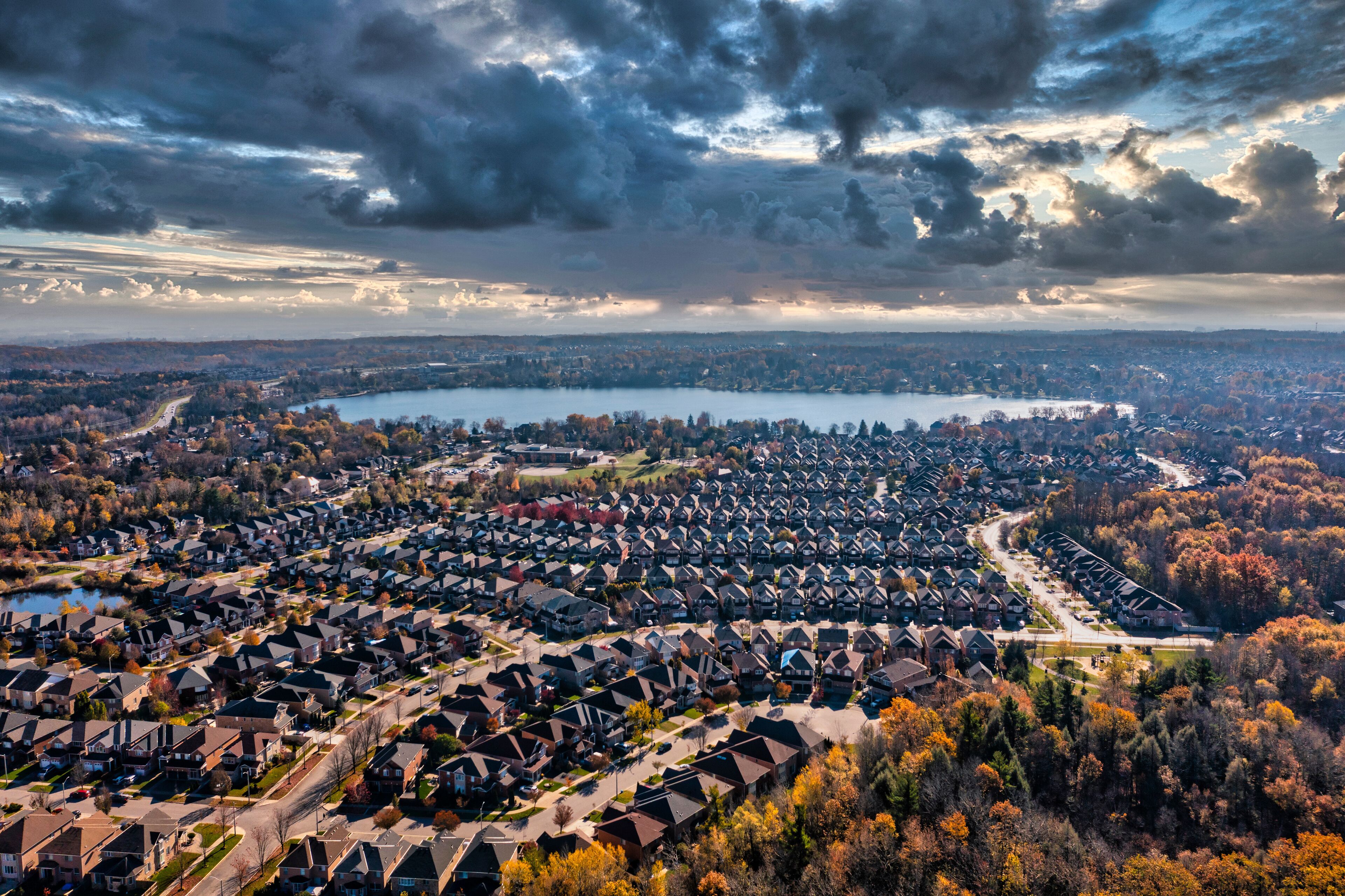 A residential area with houses, a lake, and autumn trees.