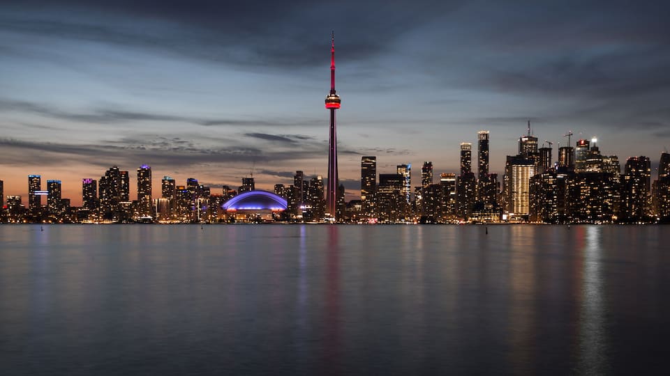 A city skyline at dusk with a prominent tower and a dome-shaped structure.