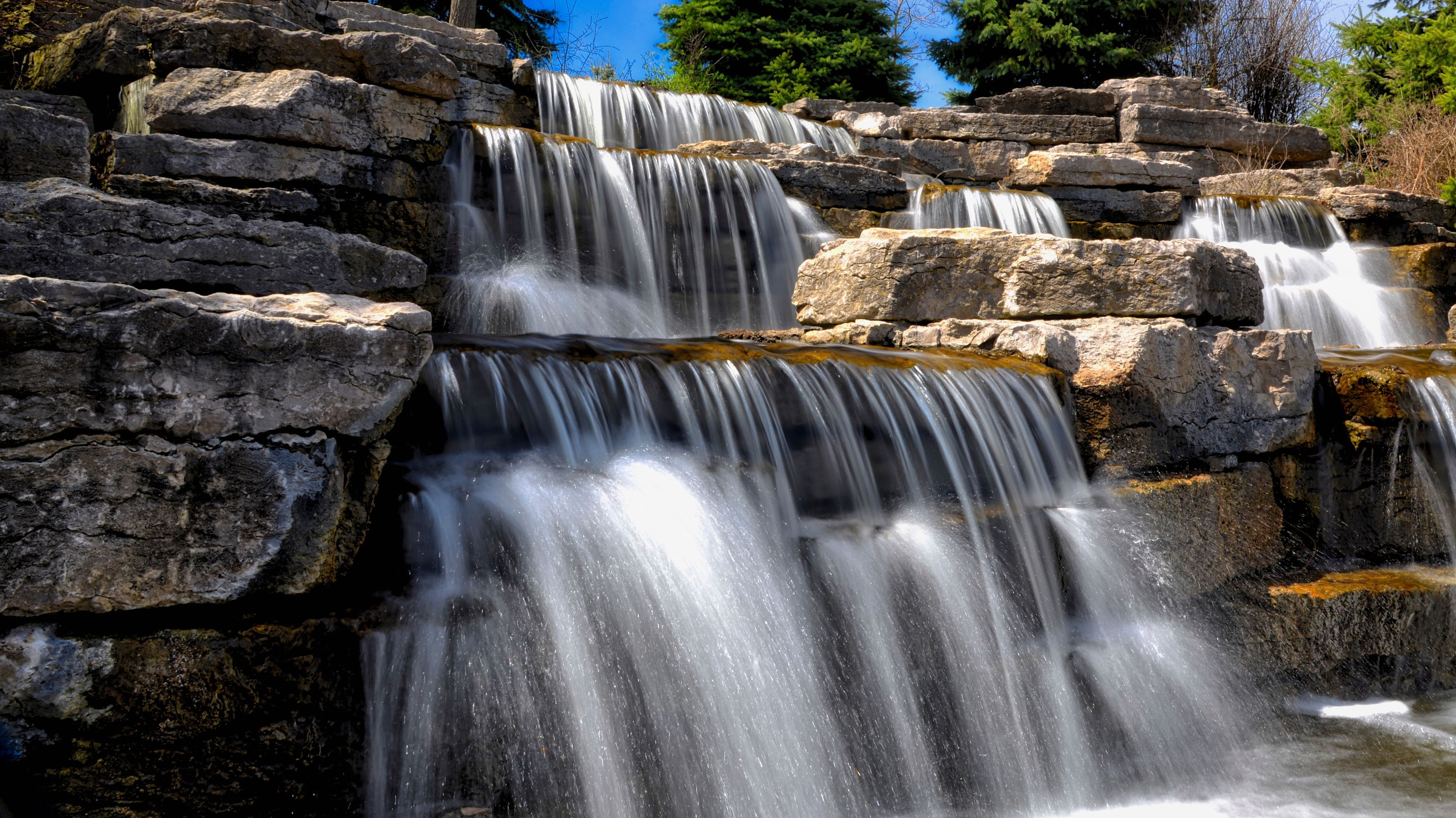 A multi-tiered waterfall cascading over rocky terrain with lush greenery in the background.