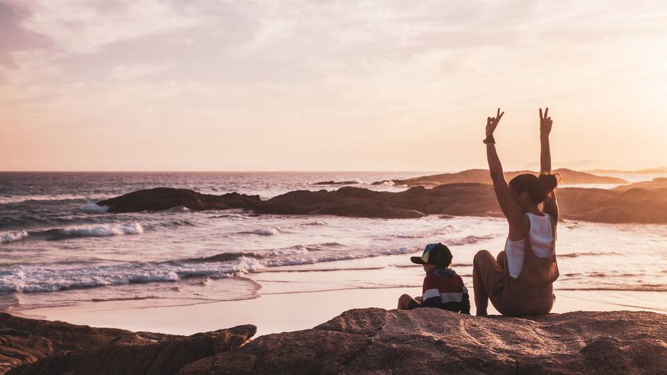 A beach with waves, rocks, and a sunset.
