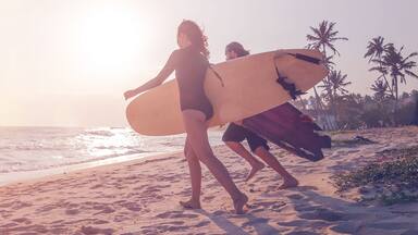 Young couple of happy smiling surfers run with surfboards on ocean coast, s panoramic banner header