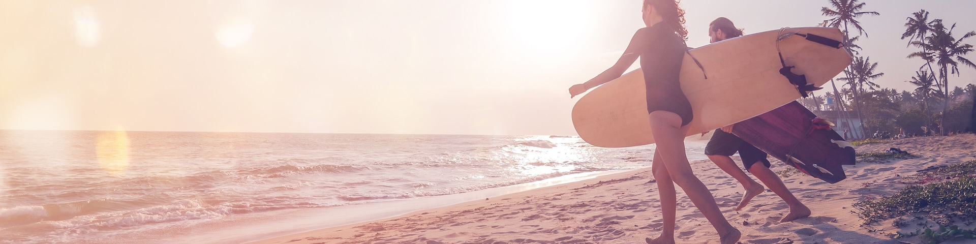 Young couple of happy smiling surfers run with surfboards on ocean coast, s panoramic banner header