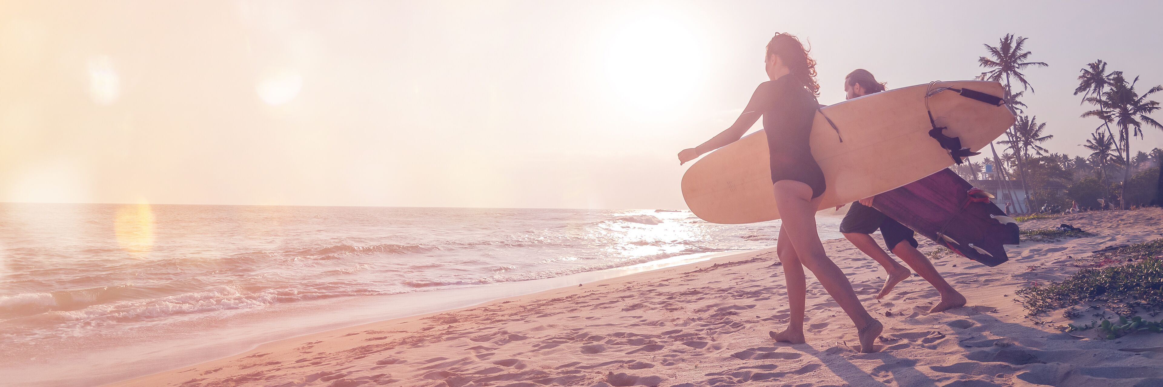 A beach with palm trees and people carrying surfboards.