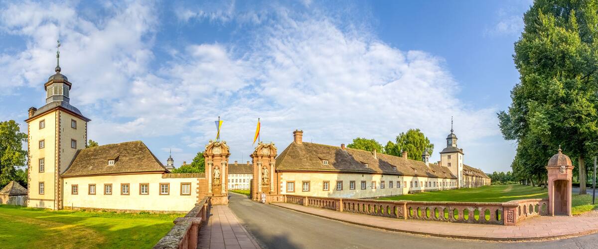 A historic building complex with a prominent tower, a large open lawn, and a well-maintained garden.