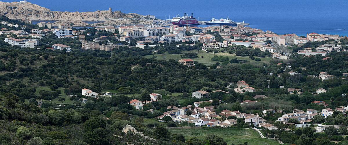A coastal town with a mix of residential buildings, a prominent red ship, and a rocky hill with a tower.
