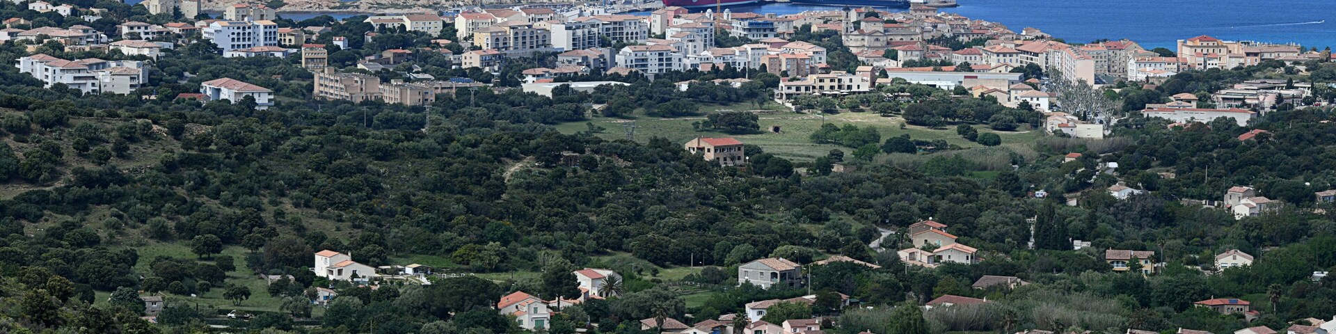 A coastal town with a mix of residential buildings, a prominent red ship, and a rocky hill with a tower.