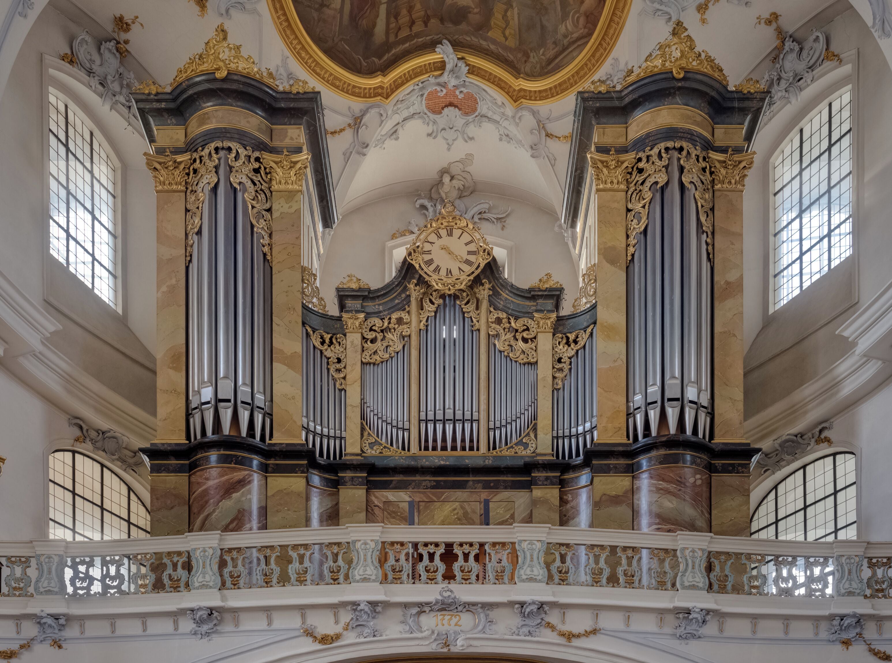 An ornate organ with gold accents and marble columns in a grand hall.