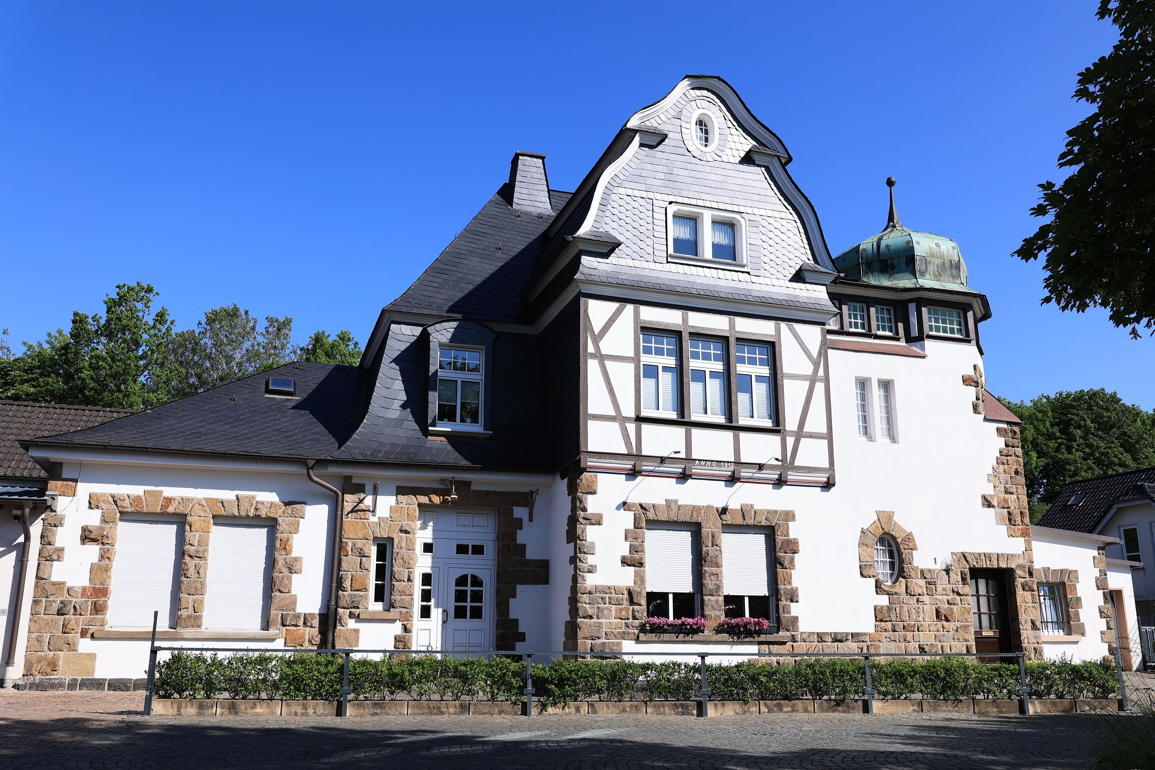 A large, historic house with a steep gable roof, stone foundation, and a small green dome.
