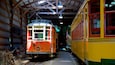 An orange and yellow vintage tram inside a covered structure with a wooden ceiling and metal beams.