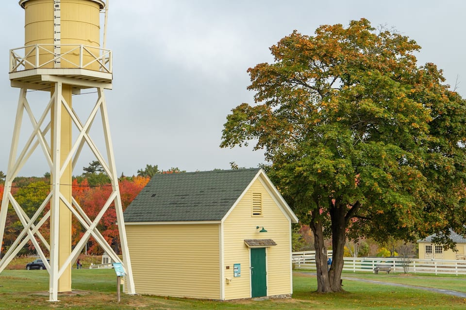 A water tower, a small yellow building, and a large tree with autumn foliage.