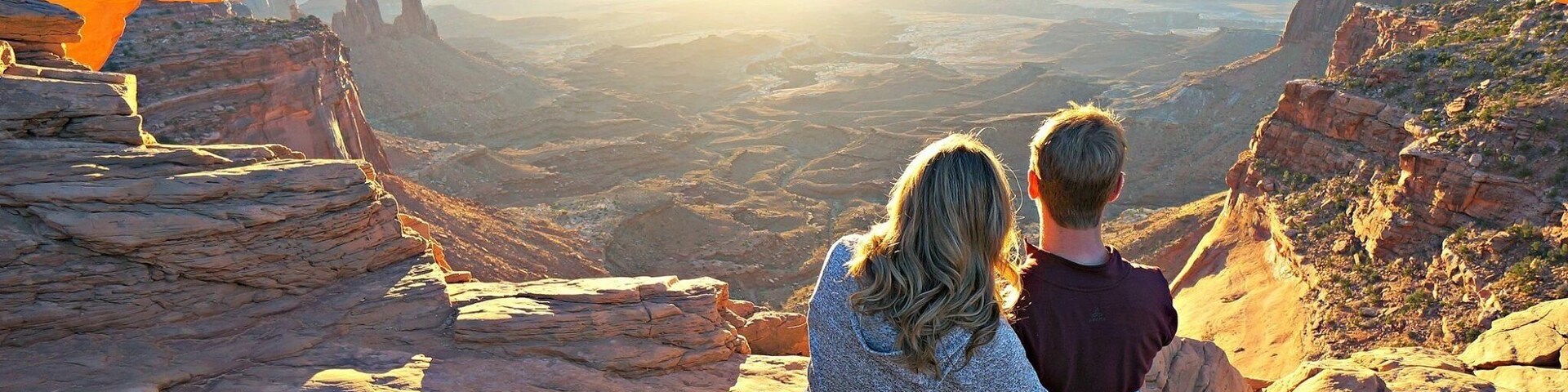 Una pareja sentada sobre una roca con vista a un cañón que tiene una formación arqueada.
