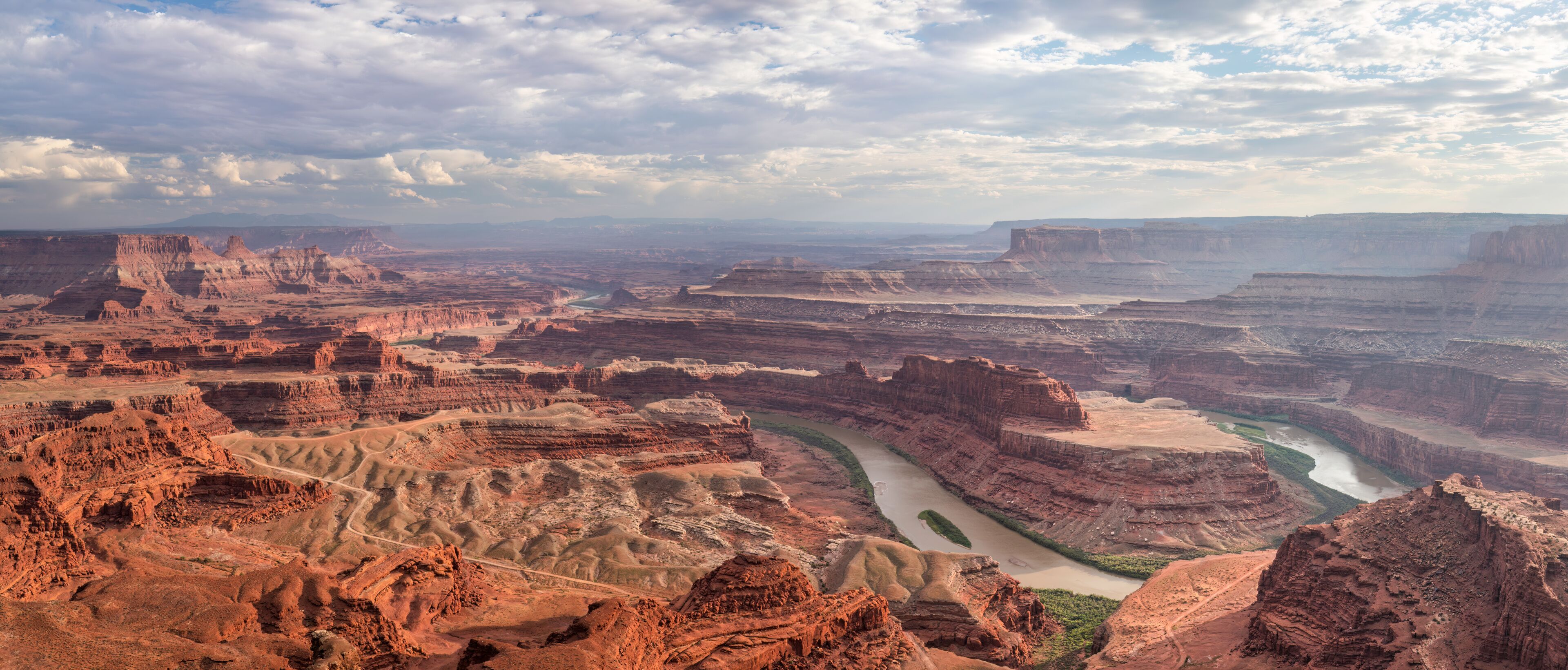 A canyon landscape with a river, layered rock formations, and a cloudy sky.