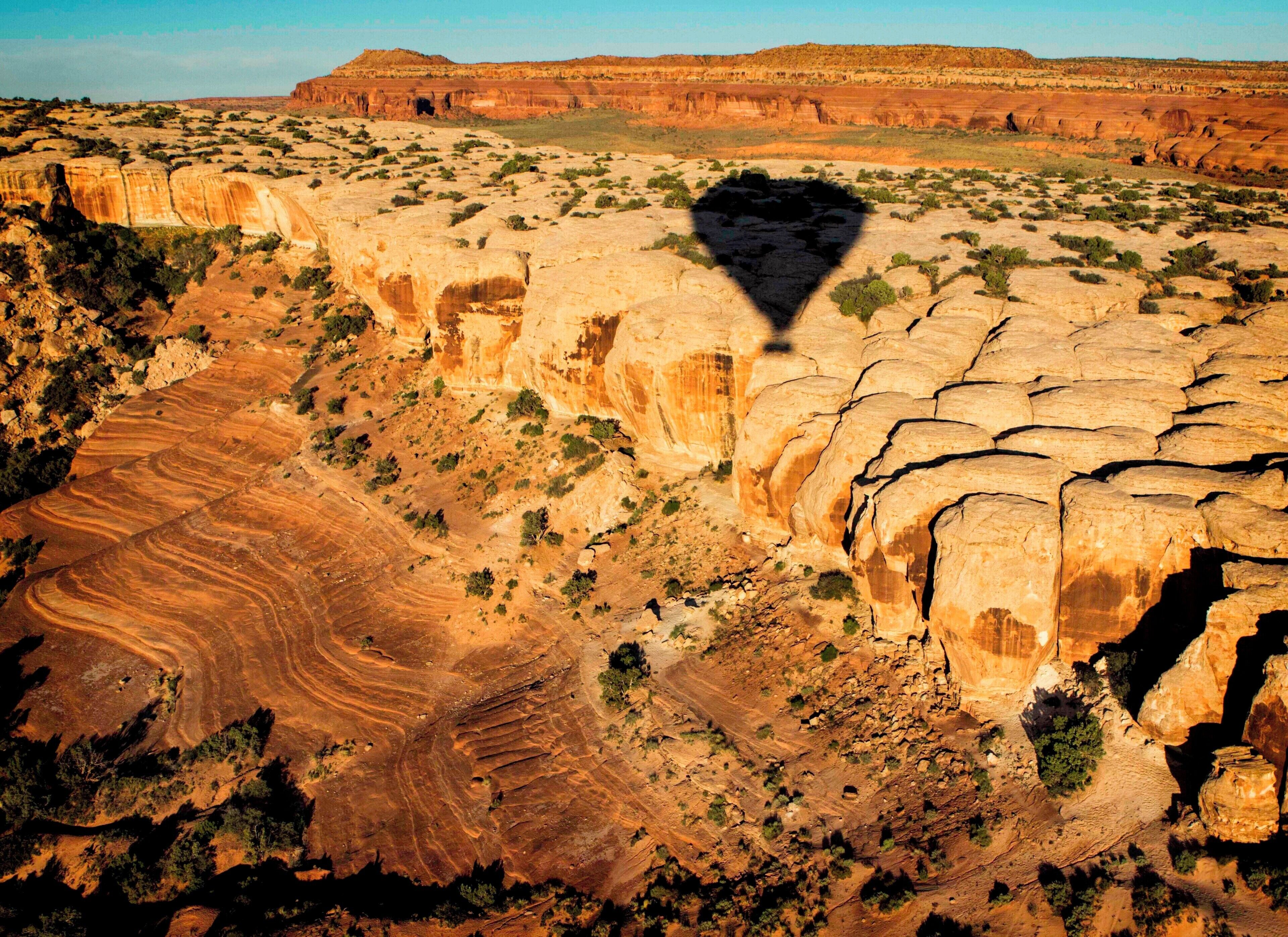 A vast canyon with layered rock formations and sparse vegetation.