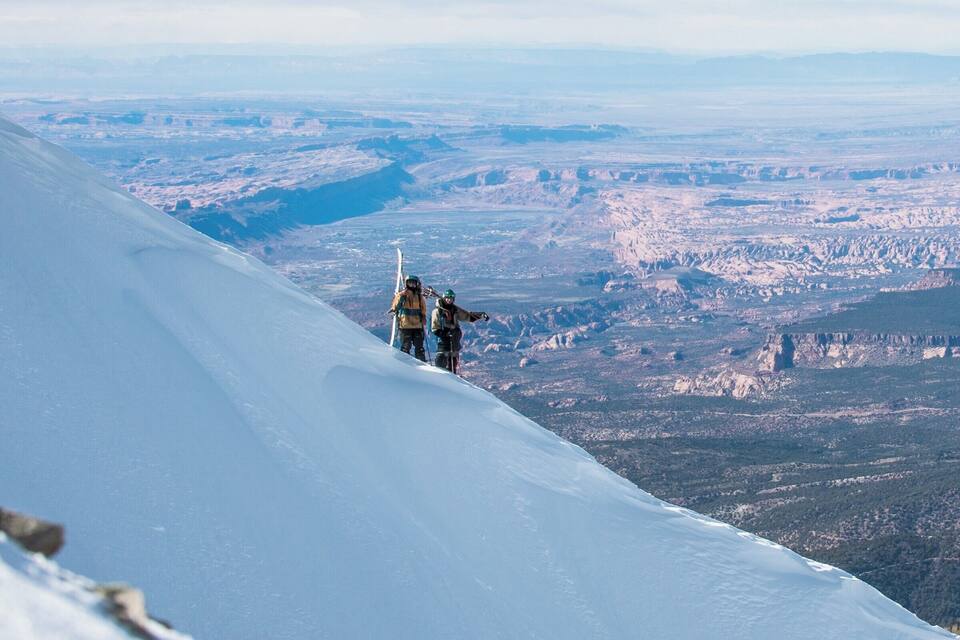A snowy mountain slope with two skiers descending.