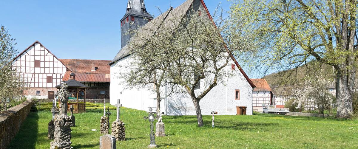 A church with a tall steeple, a white building with a red roof, and a cemetery with stone crosses.