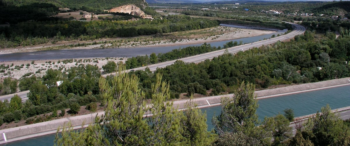 A river with a bridge, surrounded by greenery and hills.