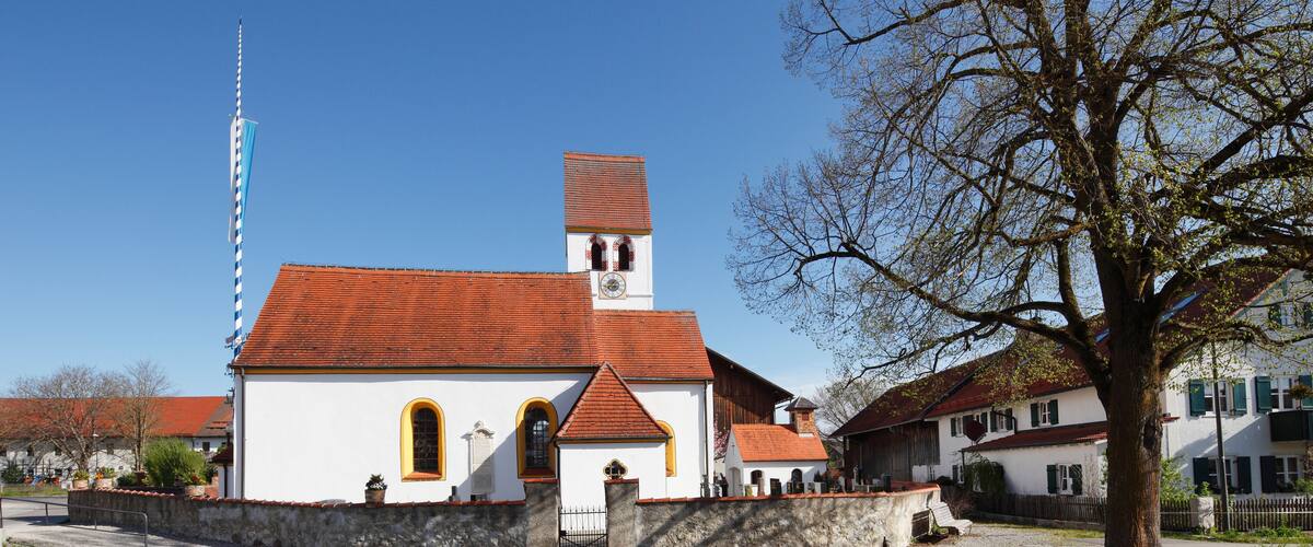 A church with a red roof and white walls, a tall tower, and a large tree in the foreground.