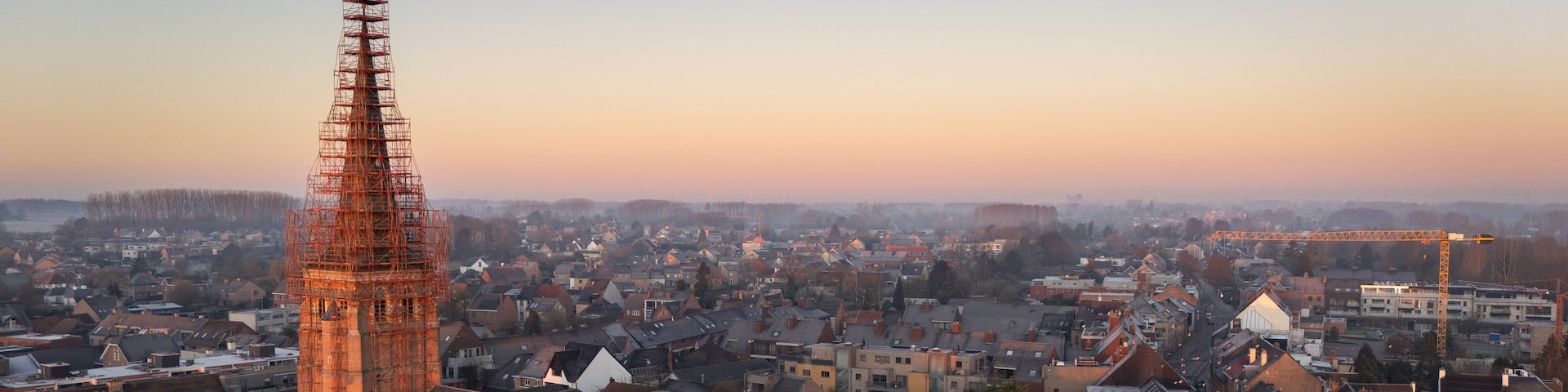 aerial view, drone view of the Sint-Servatiuskerk church in Diepenbeek, Belgium. The tower is standing in construction scaffolding for renovation of the tower. Early morning sunrise during winter.