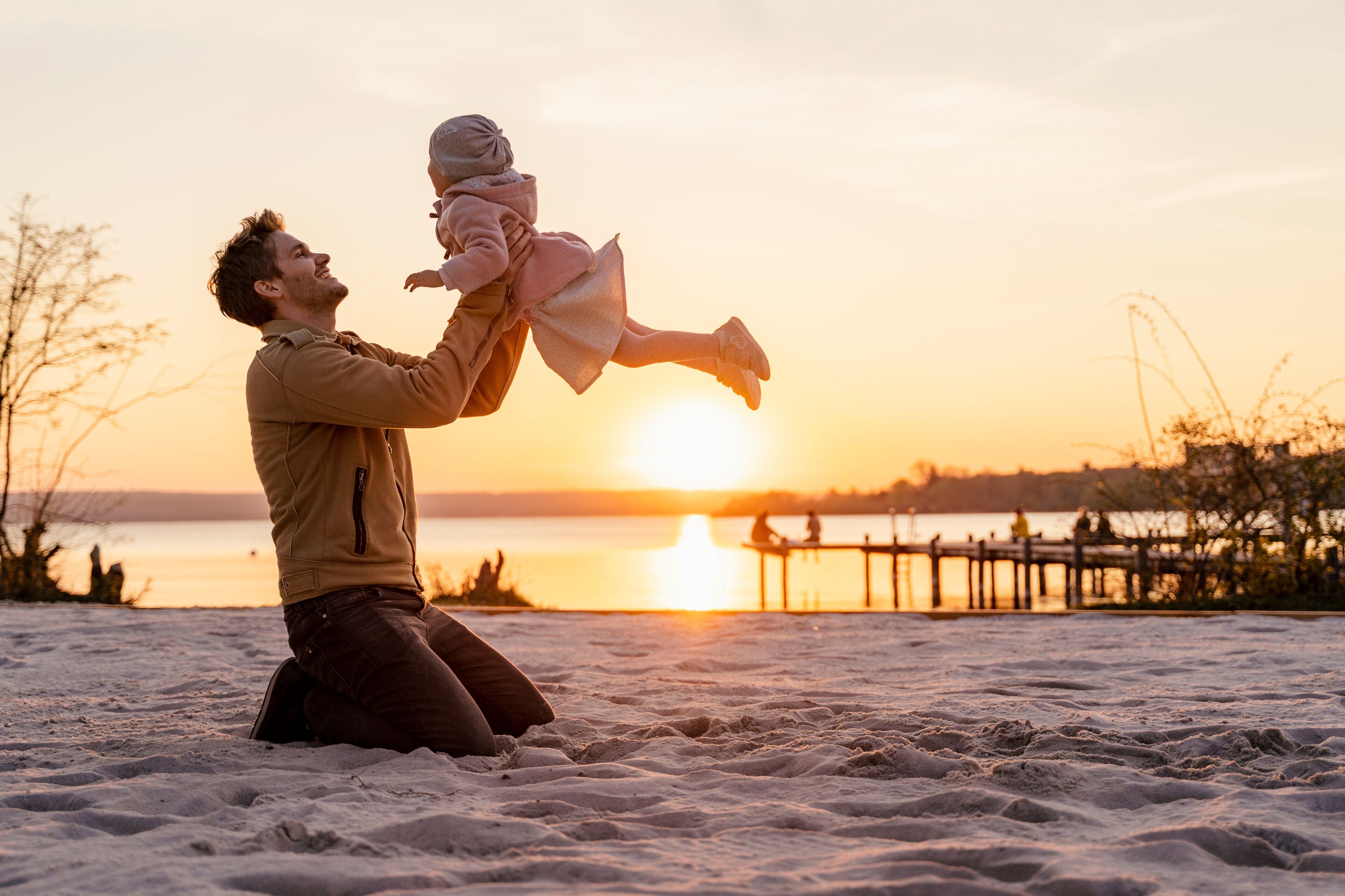 A beach scene with a sunset, sand, and a wooden pier in the background.