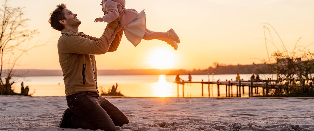 Une scène de plage avec un coucher de soleil, du sable et une jetée en bois en arrière-plan.