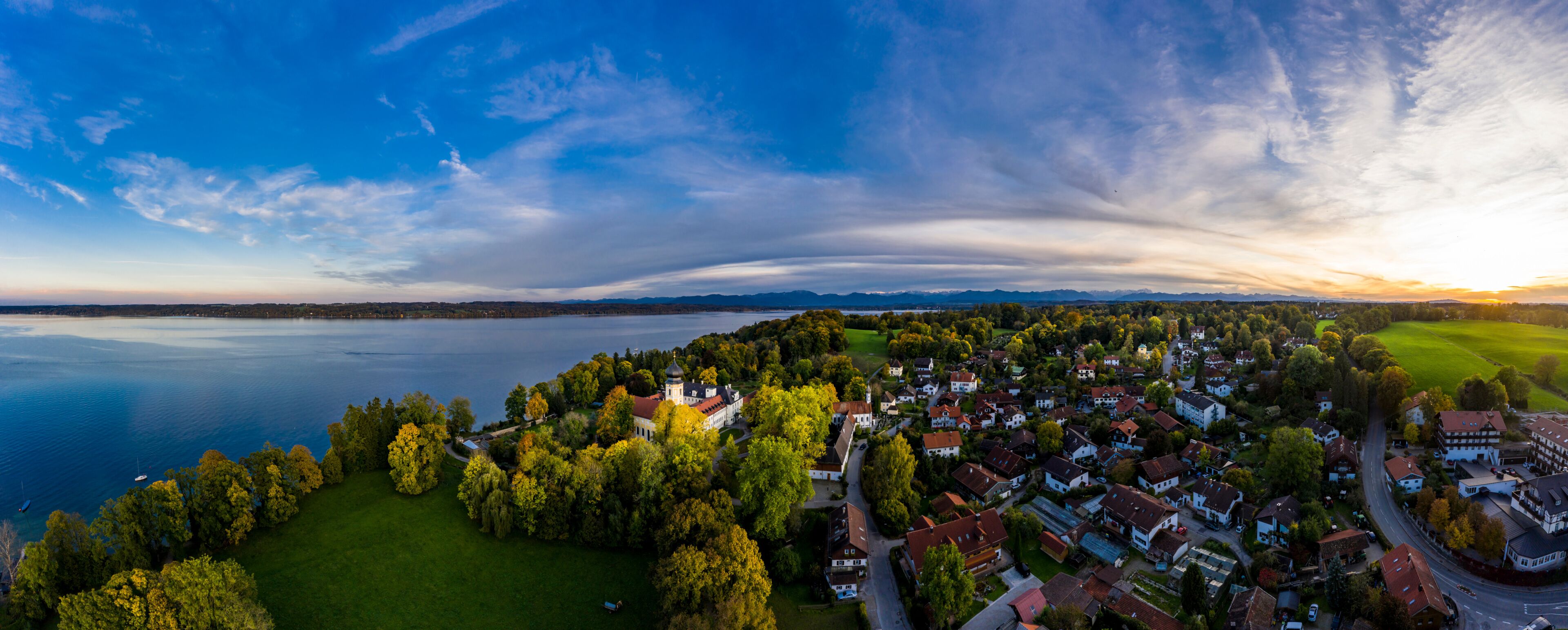 A lakeside town with a prominent church, dense greenery, and a clear sky.