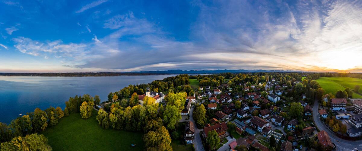 A lakeside town with a prominent church, dense greenery, and a clear sky.