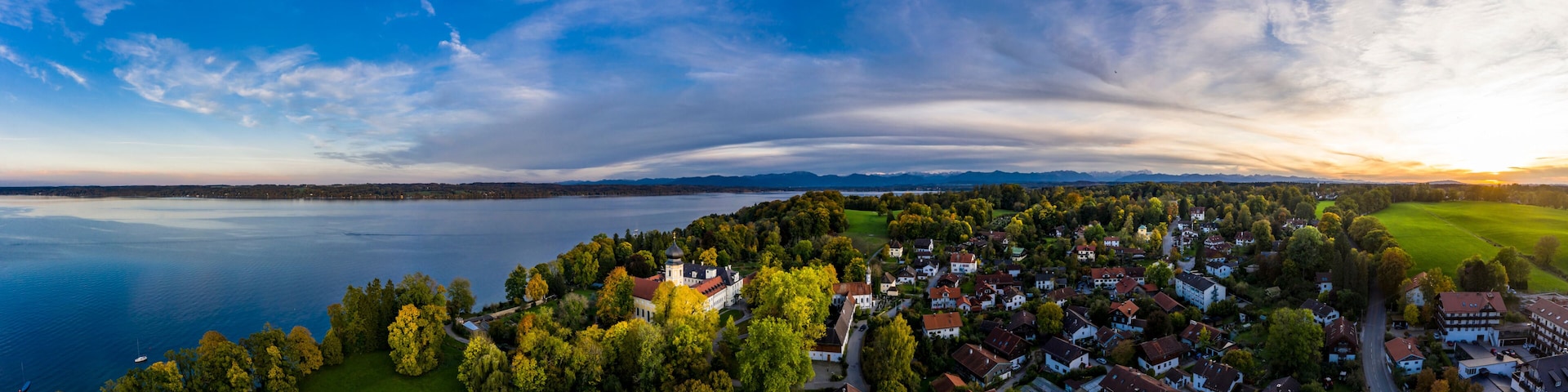 A lakeside town with a prominent church, dense greenery, and a clear sky.